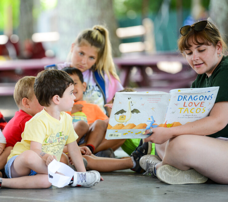 A Summer Trails staff member reading a book to a camper.